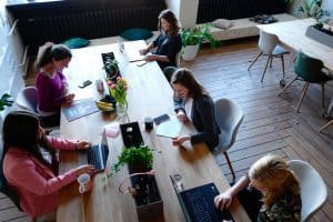 Five women sat at a long wooden desk. They are working on laptops.